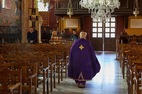 A priest in a purple robe walks through the empty pews of a church, Church of the Annunciation of
