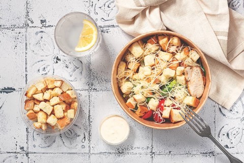Caesar salad in a paper container, take it on the way, with sauce and croutons, on the table,