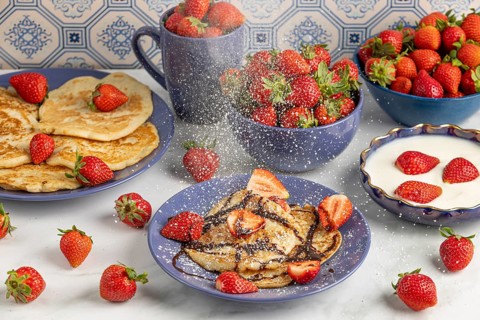 Icing sugar falls on pancakes with strawberries and chocolate syrup, fresh strawberries and yoghurt