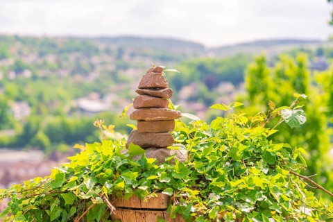 A stone tower sits on ivy, surrounded by green nature and an urban background, Panorama Holzsteg,