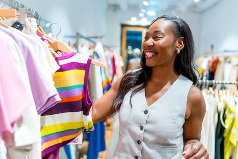 Happy customer smiling while examining a colorful striped top in a vibrant clothing store, enjoying