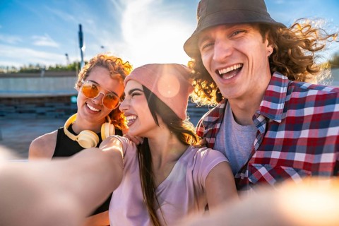 Three cheerful young friends taking a selfie outdoors, soaking up the sun and enjoying a vibrant