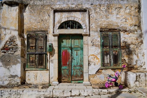 Weathered old house facade in an urban environment, pink pram in front of it, Symi Town, Symi,