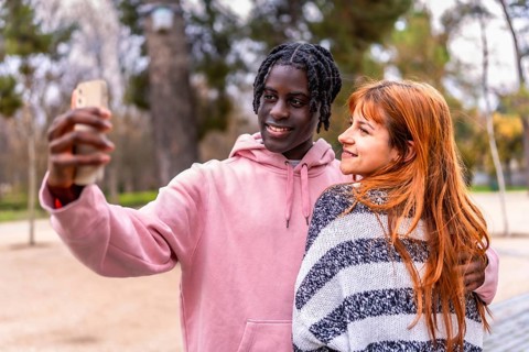 Young multiracial couple smiling together while capturing a joyful selfie with a smartphone in a