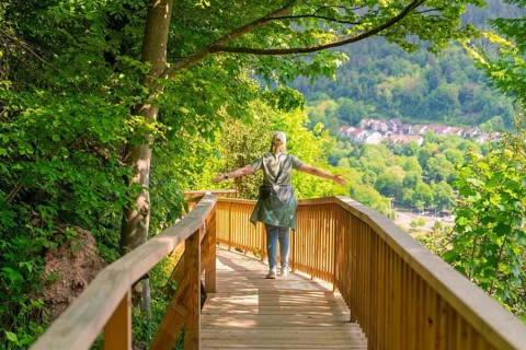 A person walks on a wooden path with outstretched arms through nature, Panorama Holzsteg, Calw,