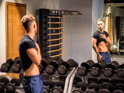 Young Shirtless Handsome Muscular Man Admiring His Muscles in Gym Mirror or Checking Progress and