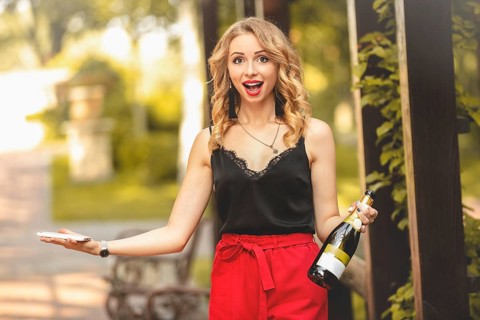 Happy young attractive white woman laughing joyfully, talking on the phone, holding a bottle of