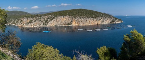 A panorama view of a small ocean cove on the coast of the Peloponnese in Greece with aquaculture