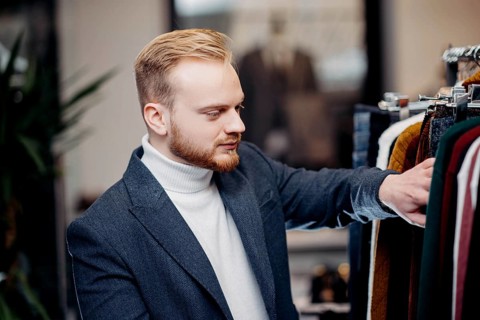 A focused man browses jackets in a clothing store, conveying a sense of style and interest