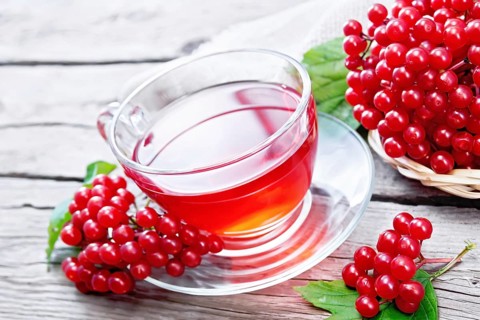 Tea with viburnum in a glass cup, green leaves, wicker plate with berries and burlap on wooden