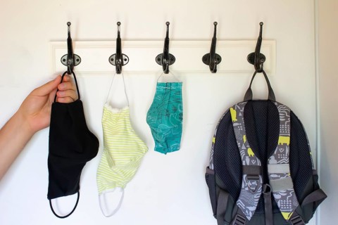 A person about to get a face mask form a Wall Hook or Coat Rack on a white wall