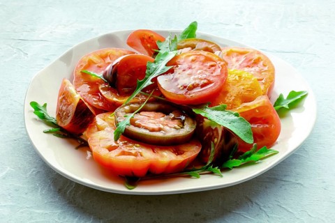 Fresh tomato and rocket salad. A variety of tomatoes of different sorts with arugula leaves.
