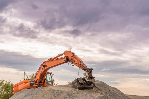 Heavy orange excavator with big bucket working on top of a ballast pile