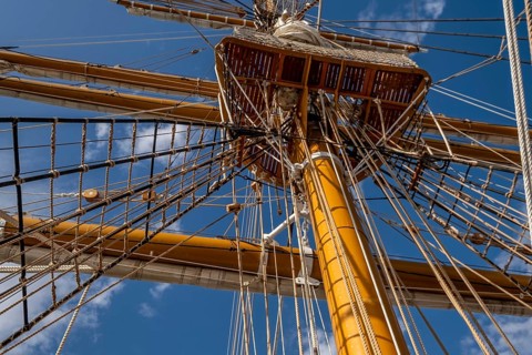 Low angle view of sailboat wooden ship masts and rigging under blue sky with clouds