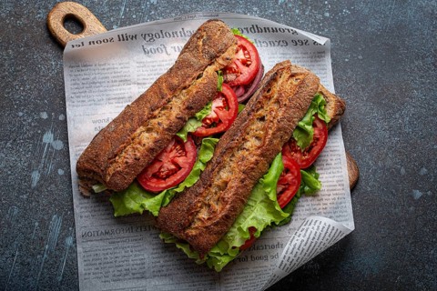 Two dark ciabatta sandwiches with green salad, ripe red tomatoes, onion and tuna on rustic concrete
