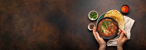 Female hands holding a bowl, eating traditional Indian Punjabi dish Dal makhani with lentils and