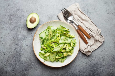 Healthy vegan green avocado salad bowl with sliced cucumbers, edamame beans, olive oil and herbs on