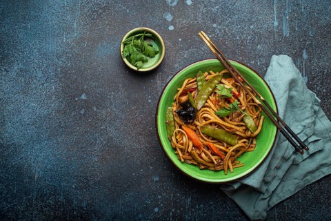 Asian stir fry udon noodles with chicken, vegetables, mushrooms in green ceramic bowl with wooden
