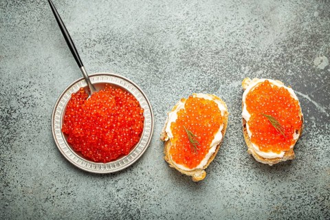 Small metal plate with red salmon caviar and two caviar toasts canape on grey concrete background,