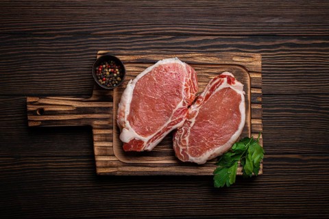 Cut raw meat pork steaks with seasonings on kitchen cutting board, rustic wooden background top