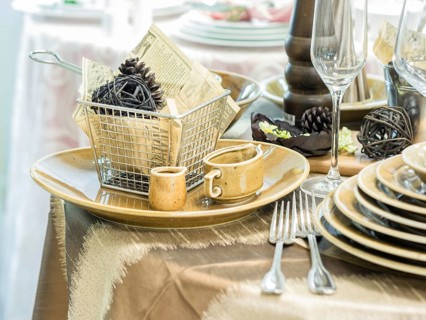 Set of new dishes on table with tablecloth. Stack of beige plates and wine glasses on restaurant