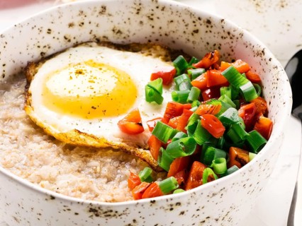 Savory oatmeal in craft trendy bowl, served with vegetables and fried egg on white concrete