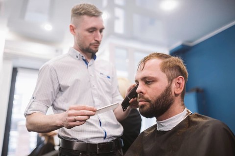 Close up shot of a man getting a trendy haircut at a hair salon. Male caucasian hairdresser serving