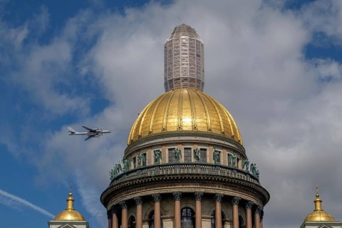 Historic building with golden dome and a passing aeroplane in the blue sky with clouds, saint