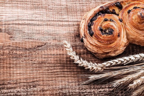 Roll with raisins wheat ears on oak wooden board food and drink concept
