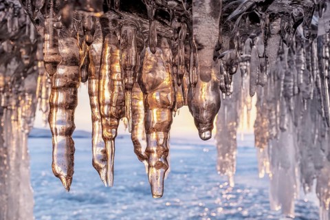 Ice cave on Baikal lake in winter. Blue ice and icicles in grotto in the sunset sunlight. Olkhon
