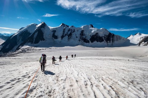 Group of Mountaineers with Backpacks is Roped Together and Ascending on Glacier in Snowy Mountains