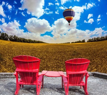 Huge balloon flies over a field. Convenient red chairs in a wheat field. The concept of eco-tourism