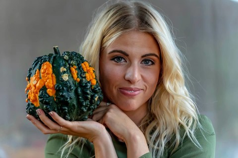 A stunning blonde model poses in a vibrant pumpkin field, wearing a stylish autumn outfit with a