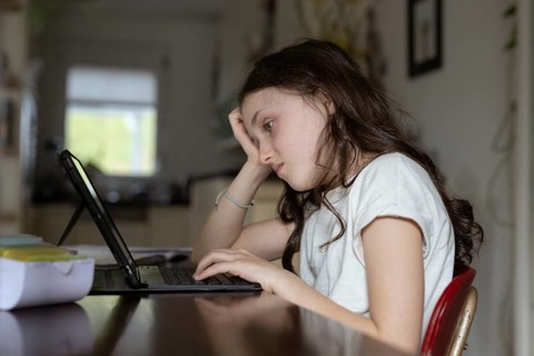 Girl, 10 years old, sits at the table with a tablet and learns