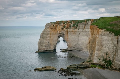 Landscape photo of tall, steep limestone cliffs by the ocean with one with a hole in it creating an