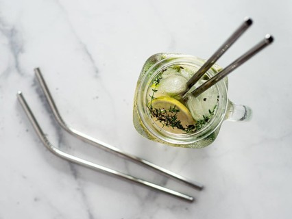 Metal drinking straws and cold drink in glass mason jar on white marble background. Top view or