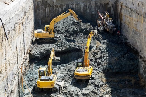Excavators dig at a construction site of a street and a subway. Baggers transport dirt to a higher