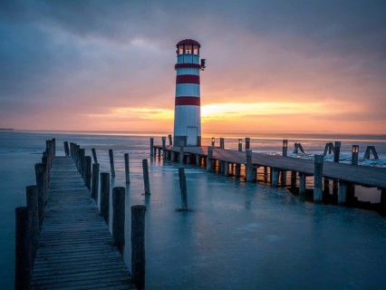 Winter landscape with lighthouse on a lake at sunset