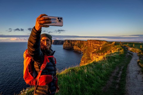 Female hiker taking a selfie, Cliffs of Moher, The Burren, County Clare, Ireland, United Kingdom,