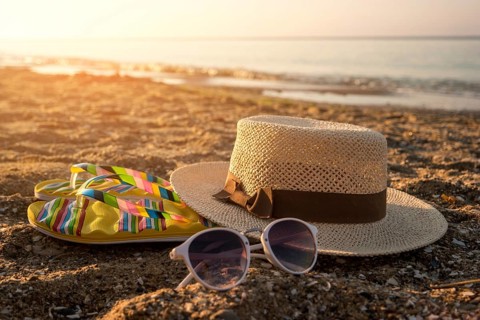 Hat with sunglasses on sand. Flip flops near the sea. The beach is calling. It's time to relax