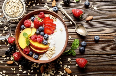 Flat lay of fruit healthy muesli with peaches strawberry almonds and blackberry in clay dish with