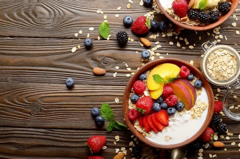 Flat lay of fruit healthy muesli with peaches strawberry almonds and blackberry in clay dish with