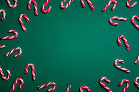 Christmas sweets frame with mini candy canes in red and white stripes, on a green paper background