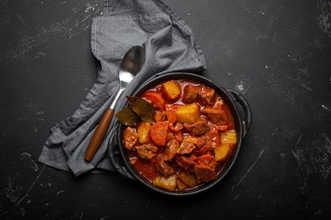 Beef meat stew with potatoes, carrot and delicious gravy in black casserole pot with bay leaves