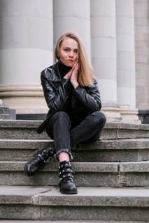 Portrait of young blonde woman with red lips wearing leather jacket on corporate building stairs.