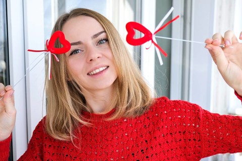 Young blonde girl in red sweater holding red hearts showing emotions. Taking selfie. Video chat.