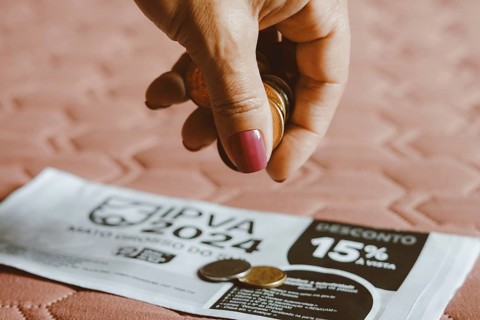 In this photo illustration, a woman counts the real money coins and, on top of the IPVA (Imposto