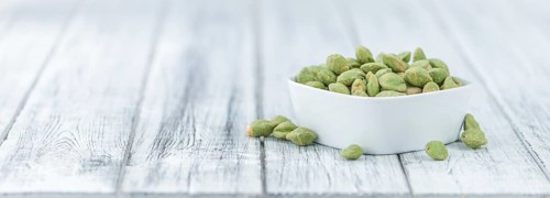 Wasabi coated Peanuts as high detailed close-up shot on a vintage wooden table (selective focus)