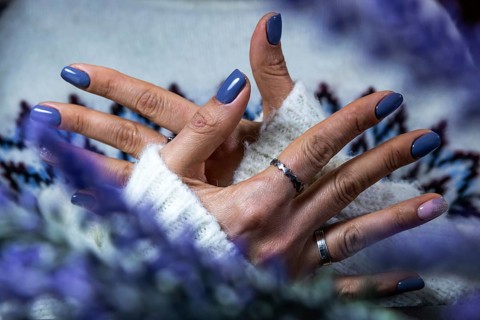 Hands showing purple manicure resting on a soft sweater, with a hint of floral elements