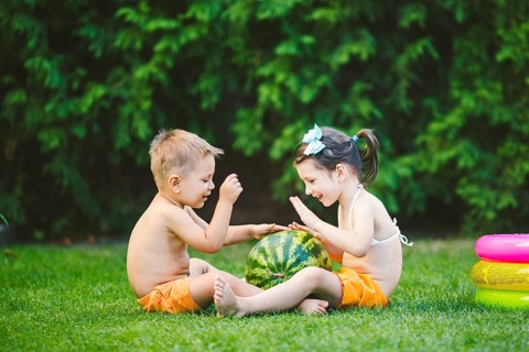 Two children, Caucasian brother and sister, sitting on green grass in backyard of house and hugging